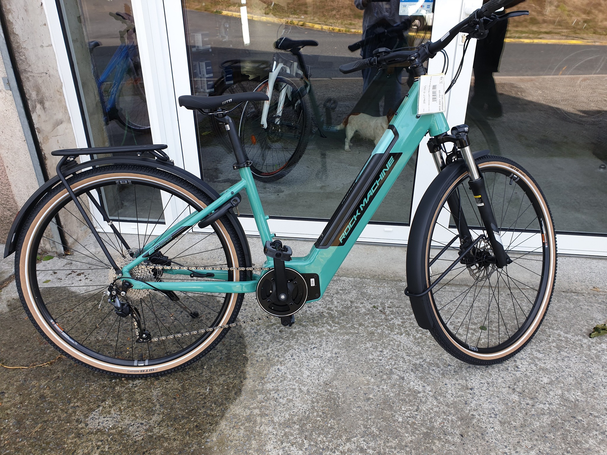 Vélo électrique vert Bicicleta-Maurandy avec batterie intégrée à lacaune-alban-brassac-81230 devant vitrine urbaine,