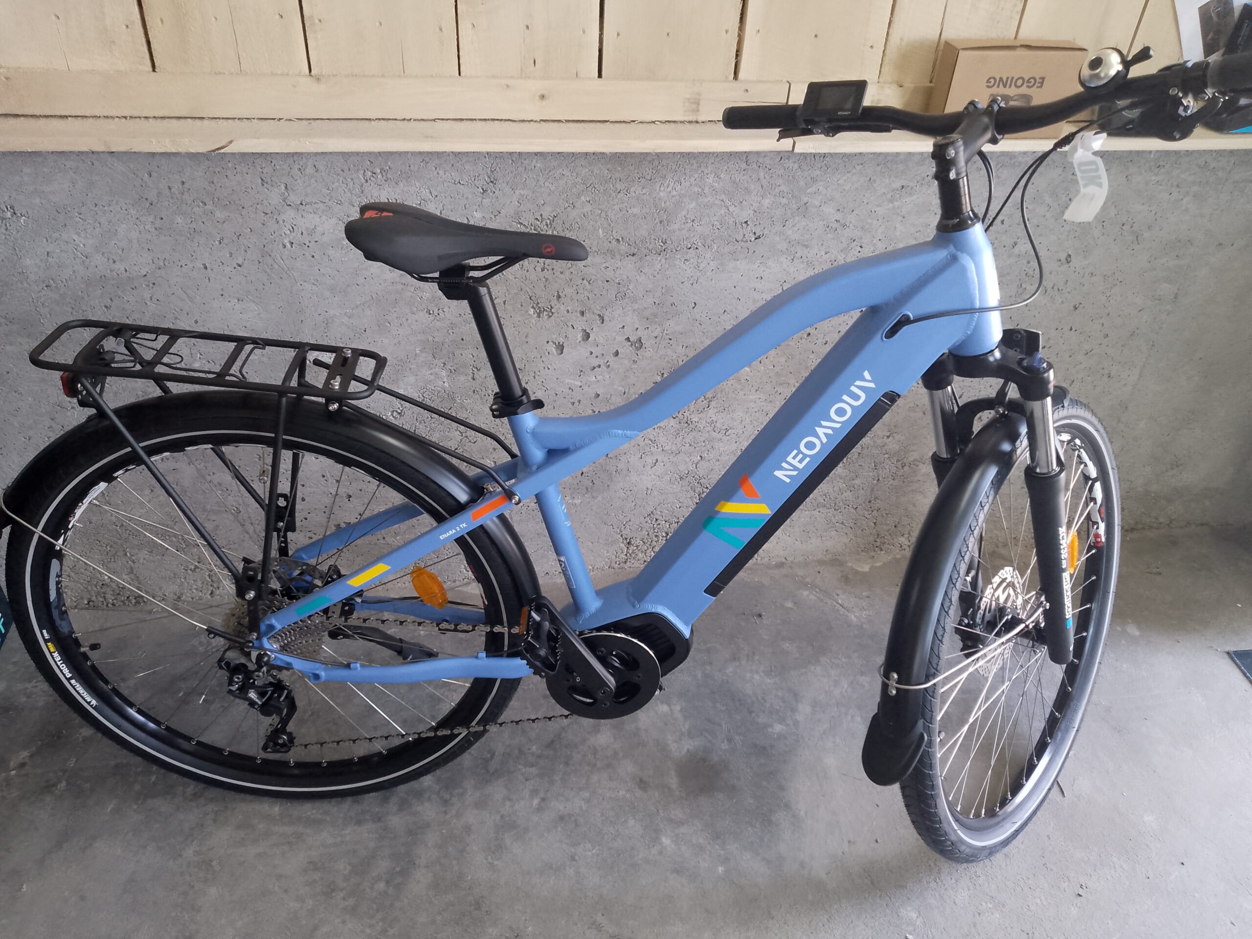Vélo électrique NEOMOUV chez Bicicleta-Maurandy, lacaune-alban-brassac-81230, bleu mat avec porte-bagages et fourche suspendue,