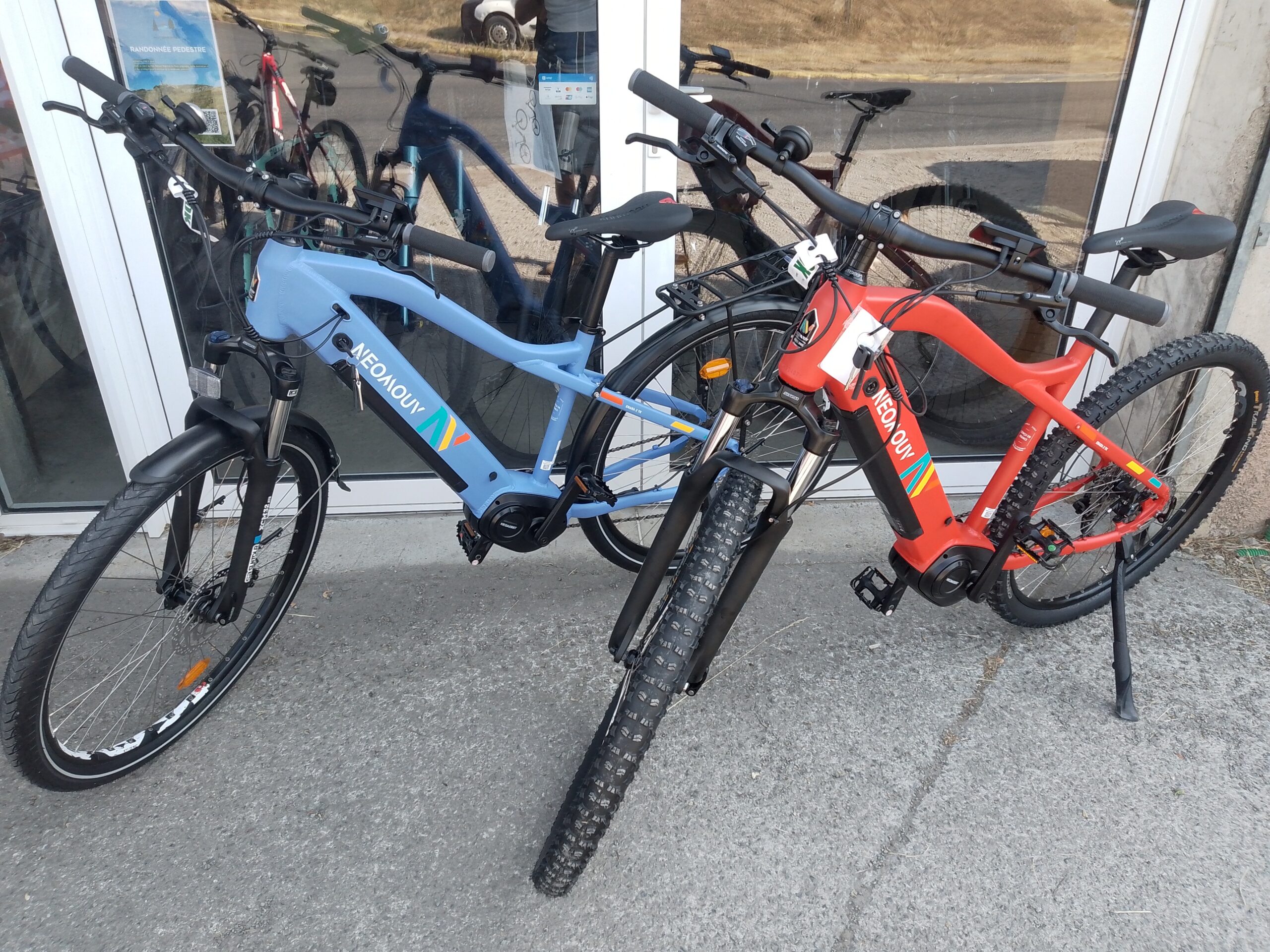 Vélos électriques NEOMOUV bleu et rouge chez Bicicleta-Maurandy à lacaune-alban-brassac-81230 devant une vitrine,